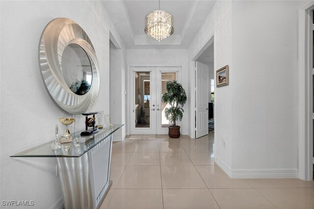 tiled foyer entrance with a raised ceiling, an inviting chandelier, and french doors