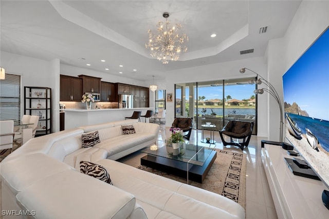 living room featuring light tile patterned floors, a water view, a tray ceiling, and a notable chandelier