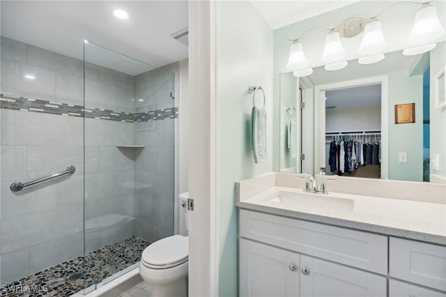 bathroom featuring a stall shower, a walk in closet, vanity, and toilet