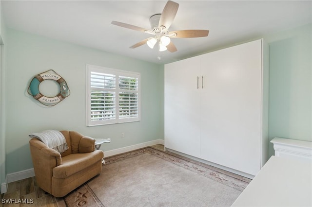 living area with a ceiling fan, baseboards, and wood finished floors