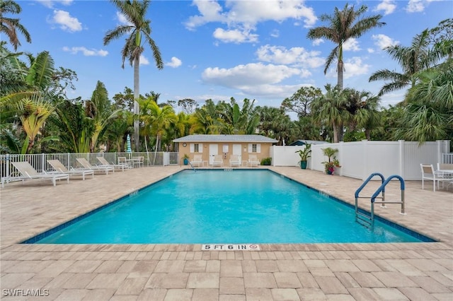 pool with a patio area, fence, and an outbuilding