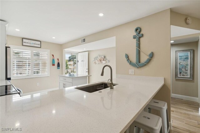 kitchen with white cabinetry, sink, kitchen peninsula, light stone counters, and a breakfast bar area