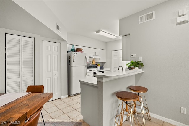 kitchen with white cabinetry, kitchen peninsula, white appliances, a kitchen bar, and light tile patterned floors