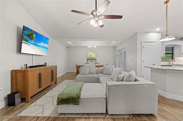 living room featuring a raised ceiling, ceiling fan with notable chandelier, and light wood-type flooring