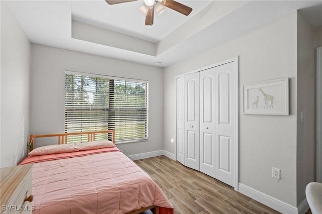 bedroom with a raised ceiling, ceiling fan, a closet, and hardwood / wood-style flooring