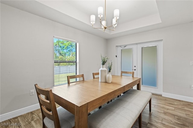 dining room featuring hardwood / wood-style flooring, an inviting chandelier, french doors, and a tray ceiling