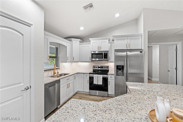 kitchen with appliances with stainless steel finishes, vaulted ceiling, white cabinetry, and sink