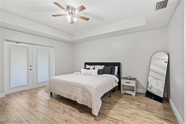 bedroom with ceiling fan, light hardwood / wood-style floors, french doors, and a tray ceiling