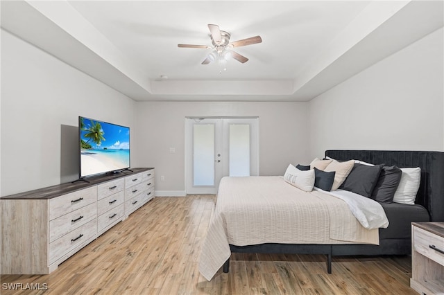 bedroom with french doors, a tray ceiling, ceiling fan, and light hardwood / wood-style floors