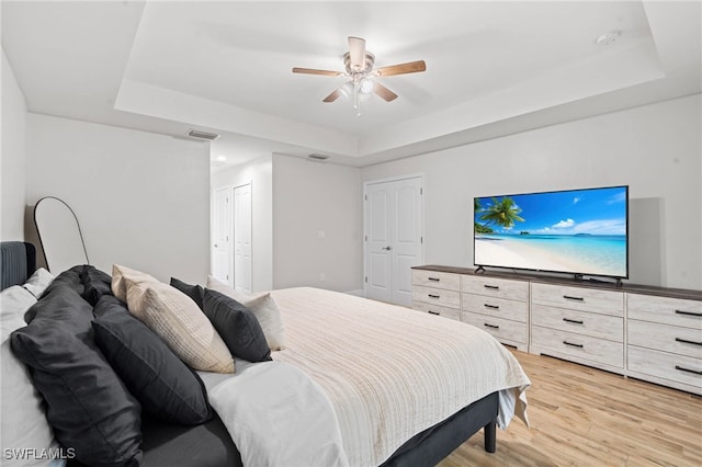 bedroom with a tray ceiling, ceiling fan, and light wood-type flooring