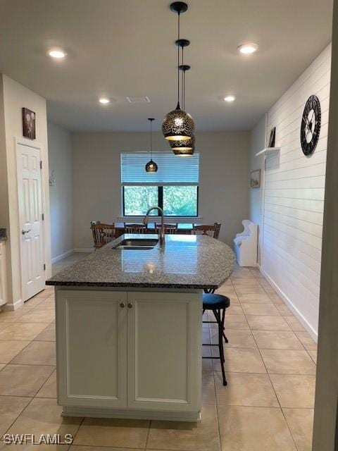 kitchen with a center island with sink, sink, dark stone countertops, light tile patterned floors, and decorative light fixtures