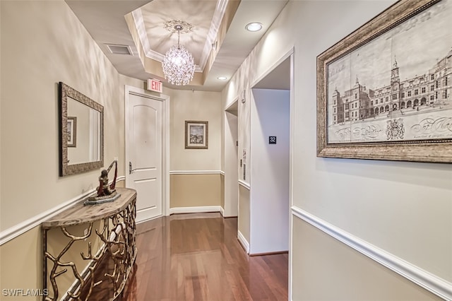 hallway with a tray ceiling, dark wood-type flooring, a chandelier, and ornamental molding