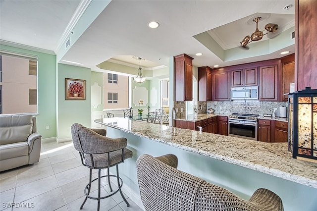 kitchen with a raised ceiling, hanging light fixtures, appliances with stainless steel finishes, light stone counters, and kitchen peninsula