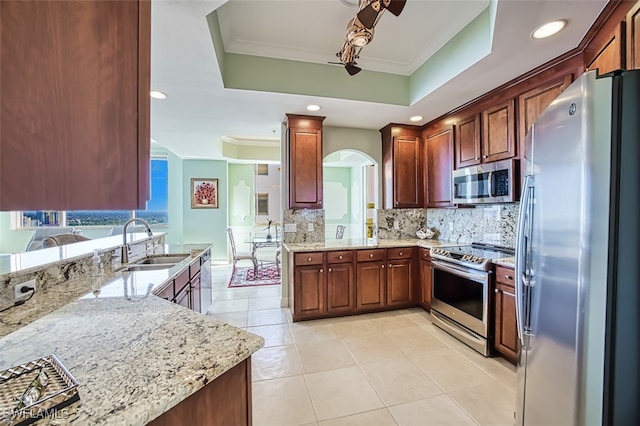 kitchen with light stone countertops, sink, stainless steel appliances, kitchen peninsula, and a tray ceiling