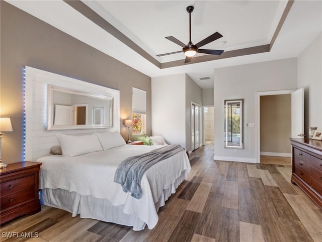 bedroom featuring hardwood / wood-style floors, ceiling fan, a raised ceiling, and crown molding