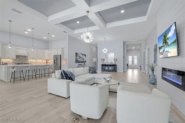 living room with a towering ceiling, coffered ceiling, beam ceiling, light hardwood / wood-style flooring, and a notable chandelier