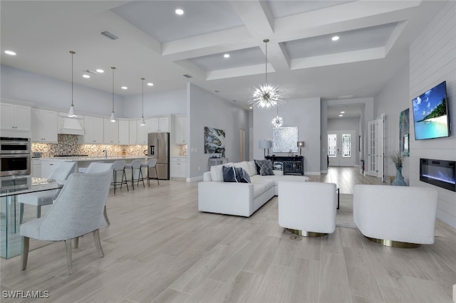 living room featuring french doors, light wood-type flooring, a towering ceiling, coffered ceiling, and an inviting chandelier