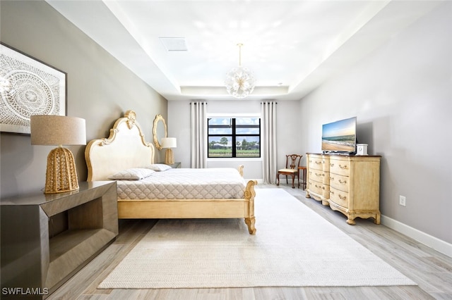 bedroom with light wood-type flooring and a raised ceiling