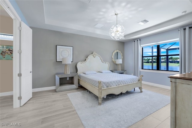 bedroom featuring a tray ceiling, light hardwood / wood-style flooring, and a chandelier