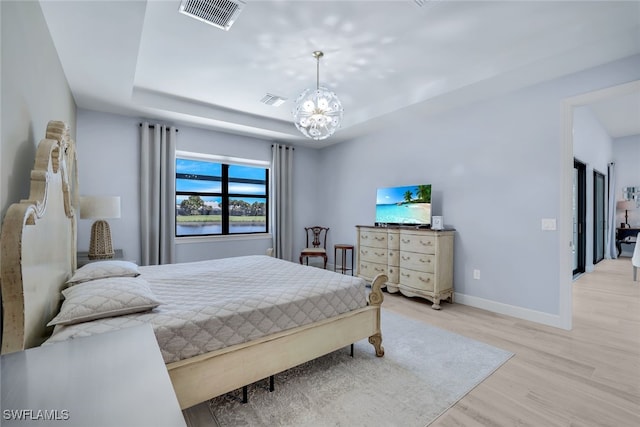 bedroom with light hardwood / wood-style floors, a raised ceiling, and a chandelier