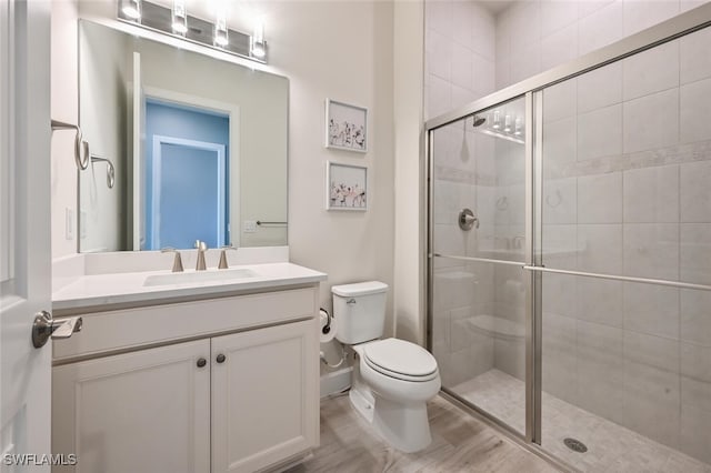 bathroom featuring wood-type flooring, vanity, toilet, and a shower with shower door