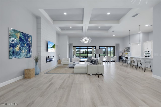 living room featuring a large fireplace, light hardwood / wood-style floors, a high ceiling, and coffered ceiling