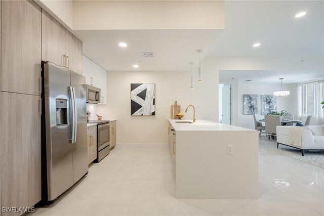 kitchen featuring light brown cabinetry, stainless steel appliances, sink, hanging light fixtures, and an island with sink