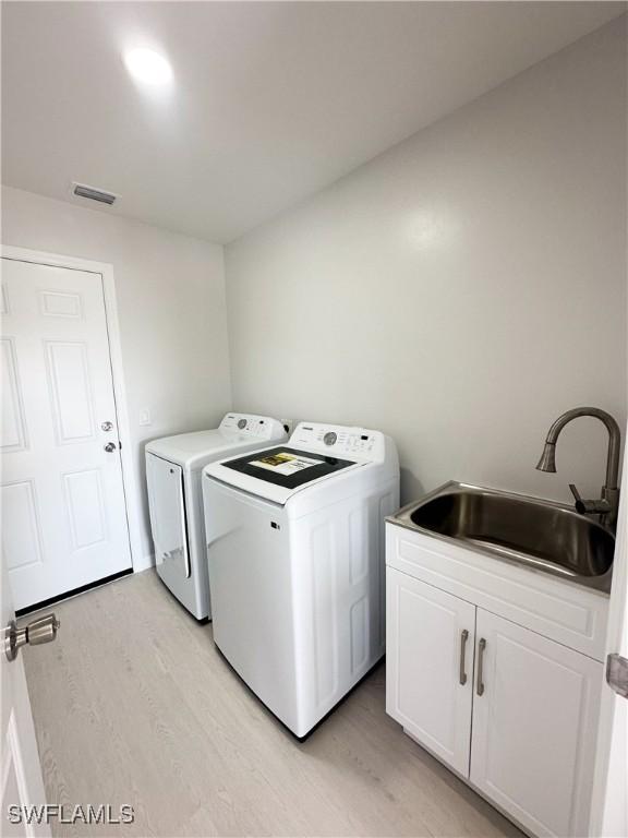 washroom with cabinets, sink, washer and dryer, and light hardwood / wood-style flooring