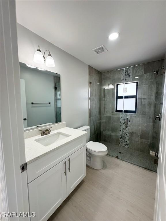 bathroom with hardwood / wood-style flooring, vanity, toilet, and an enclosed shower