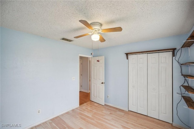 unfurnished bedroom featuring ceiling fan, a closet, a textured ceiling, and light wood-type flooring