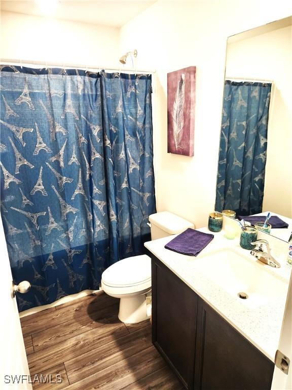 bathroom with a shower with shower curtain, wood-type flooring, vanity, and toilet