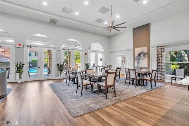 dining space featuring french doors, hardwood / wood-style flooring, ceiling fan, and a high ceiling