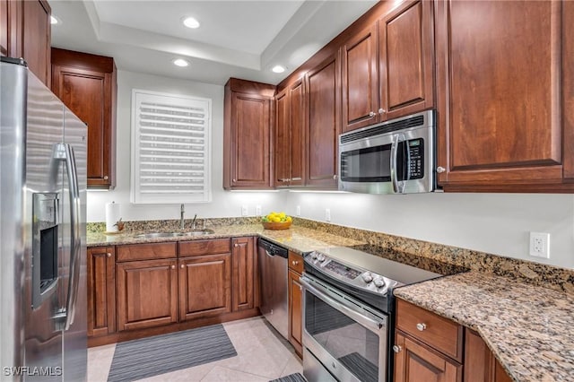 kitchen featuring sink, a raised ceiling, light stone counters, light tile patterned flooring, and appliances with stainless steel finishes