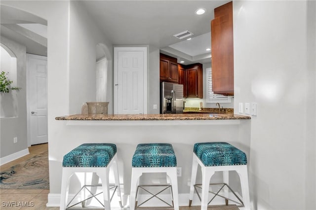 kitchen featuring kitchen peninsula, stainless steel fridge, sink, and stone counters