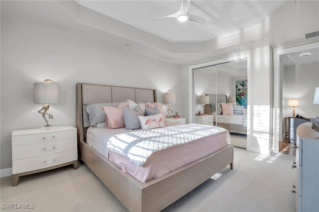 bedroom featuring light carpet, a raised ceiling, a closet, and ceiling fan