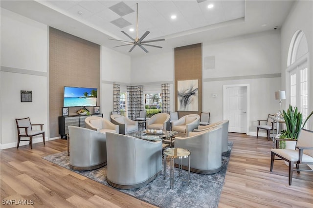 living room featuring a raised ceiling, ceiling fan, a towering ceiling, and light hardwood / wood-style floors