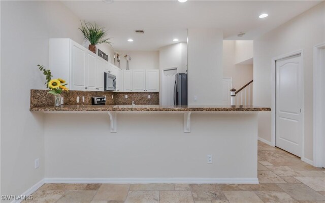 kitchen with a kitchen bar, white cabinetry, dark stone counters, kitchen peninsula, and stainless steel appliances