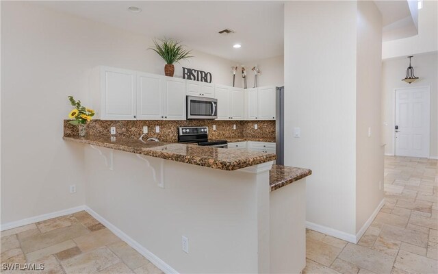 kitchen with white cabinetry, decorative backsplash, dark stone countertops, kitchen peninsula, and stainless steel appliances