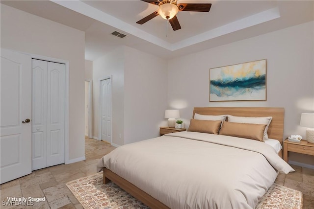 bedroom featuring two closets, a raised ceiling, and ceiling fan