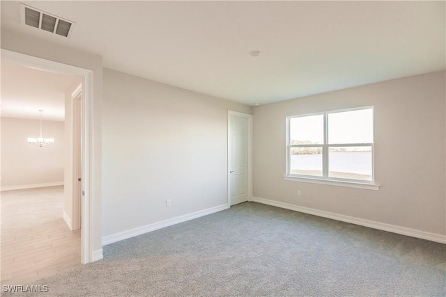 empty room with light colored carpet and a notable chandelier