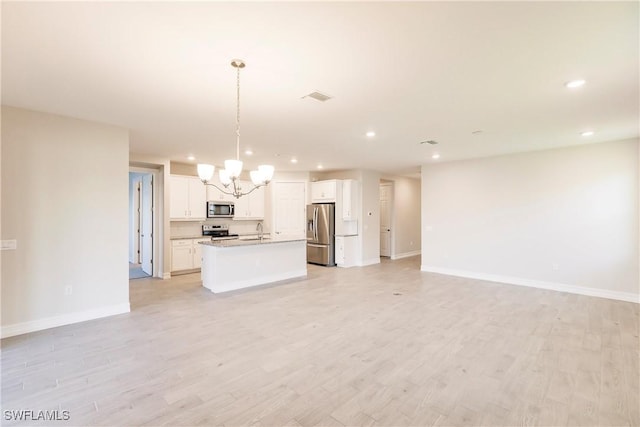 kitchen featuring a kitchen island with sink, sink, decorative light fixtures, white cabinetry, and stainless steel appliances