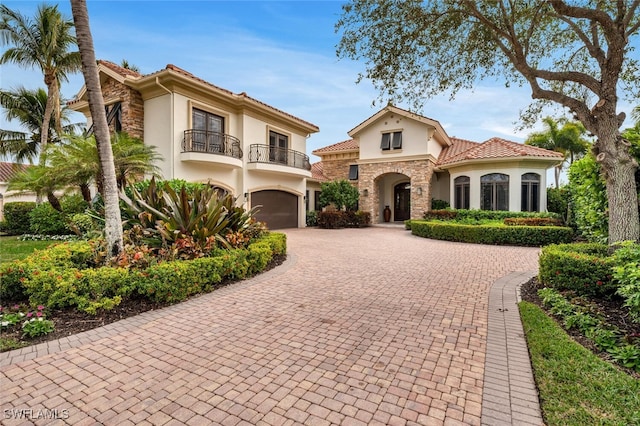 mediterranean / spanish-style home with decorative driveway, stone siding, a balcony, and stucco siding