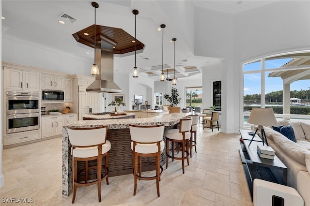 kitchen with light stone countertops, appliances with stainless steel finishes, hanging light fixtures, cream cabinets, and a breakfast bar area