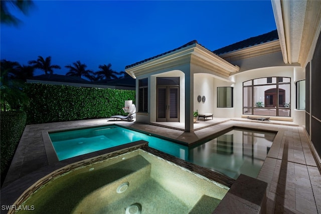 pool at night featuring a patio, french doors, a fenced in pool, and an in ground hot tub