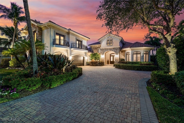 mediterranean / spanish-style house featuring stone siding, decorative driveway, a balcony, and stucco siding