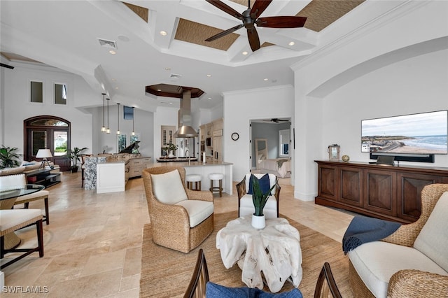 living room featuring a ceiling fan, visible vents, crown molding, and a high ceiling