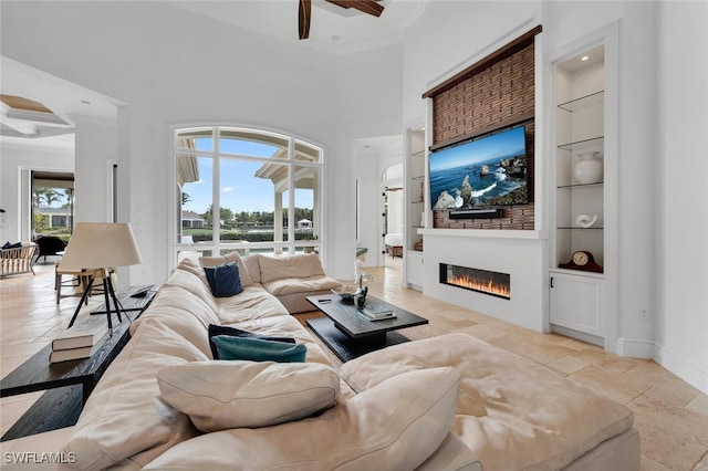 living room featuring ceiling fan, crown molding, a towering ceiling, and built in shelves