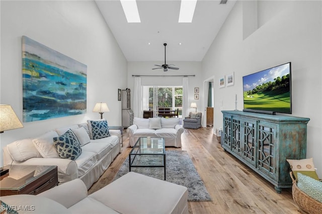 living room featuring a skylight, light hardwood / wood-style flooring, high vaulted ceiling, and ceiling fan