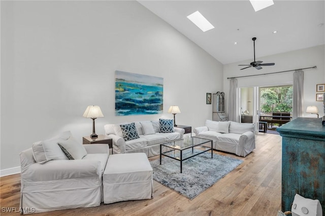 living room with ceiling fan, light hardwood / wood-style flooring, high vaulted ceiling, and a skylight