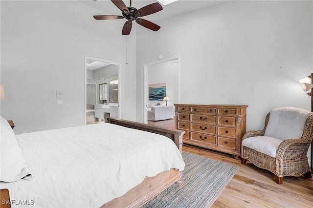 bedroom featuring ensuite bath, ceiling fan, light hardwood / wood-style flooring, and a towering ceiling